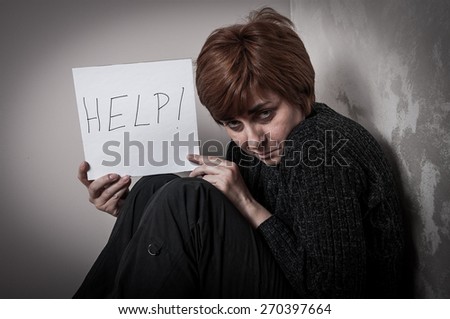 Scared and abused woman holding the paper with handwritten help sign. Low key