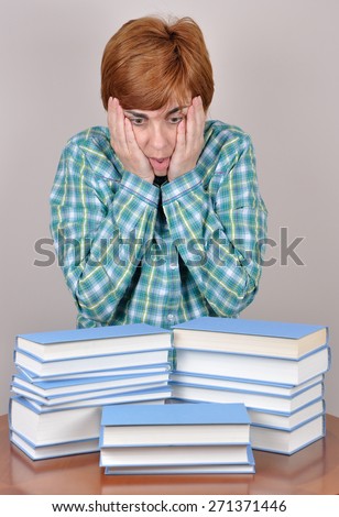 Surprised and scared  woman sitting on the brown table with books wondering how much she has to read