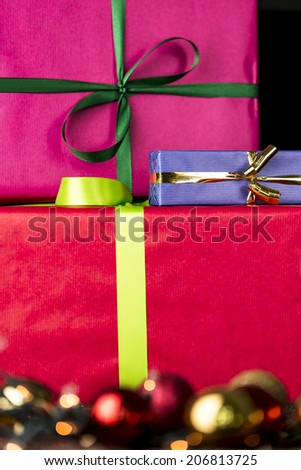 Three wrapped gifts, bowknots, spheres and glitters.  The edgy, flat surfaces of three gifts wrapped in vibrant colors contrasting with the blurry specular highlights of glitter balls in soft focus.