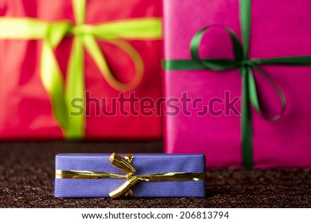 Three presents, bows and ribbons.  The golden bow and blue wrapping of a small gift box are in focus and do contrast with the red and magenta color-fields of two larger presents.