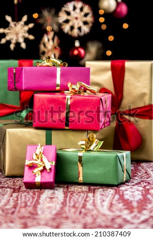 Pile of Christmas gifts wrapped in red, gold, green and magenta. Shallow depth of field. blurred stars, baubles and twinkles in the back. Xmas background with text space.