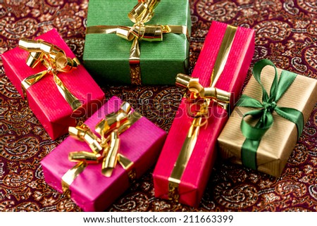 Five plain presents placed on a festive cloth. Bows in gold and green. Rich in texture. Tightly framed close-up. Fit for any gift-giving occasion.