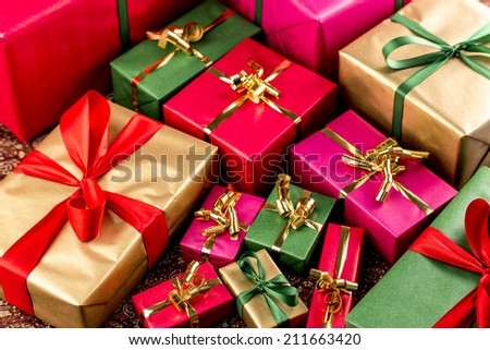 Plenty of wrapped presents in plain red, green, gold and magenta filling the frame. Shallow depth of field. Fit for any gift-giving occasion.