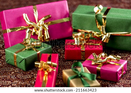Seven presents wrapped in plain red, green, gold and magenta. Placed on a festive cloth. Narrow depth of field.