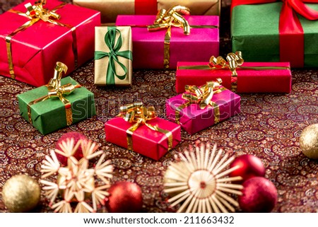 Single-colored Christmas presents placed on a festive cloth. Wrapped in red, gold, green and magenta. Straw stars and baubles in front are outside the shallow depth of field.