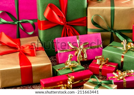 Plain-colored presents with bows in gold, red and green. Tightly framed, shallow depth of field. Background for gift-giving occasion.