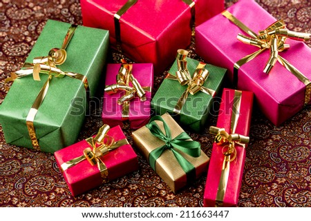 Plain-colored presents in different sizes. Wrapped in red, green, gold or magenta. Tightly framed close-up. Festive cloth with rich texture.