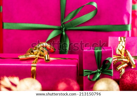 Four Christmas gifts all in plain magenta. Ribbons in gold and emerald green. Tightly framed, close up. Shortened space. Shallow depth of field. Vibrant colors. Focus on golden bow on the left.