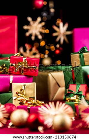 Many unicolored Christmas gifts piled up either side of the tight frame. Shallow depth of field with focus on the golden bow around the small red present. Blurred baubles and stars in front and rear.