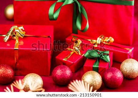 Five red Christmas presents placed on a red cloth. Bows in green and gold. Baubles and straw stars outside narrow depth of field. Tightly framed, close up. Focus on emerald bow around little red box.