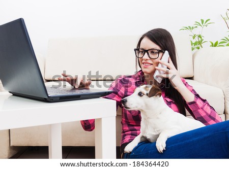 Young girl chatting on mobile phone, using computer  with pet dog in lap