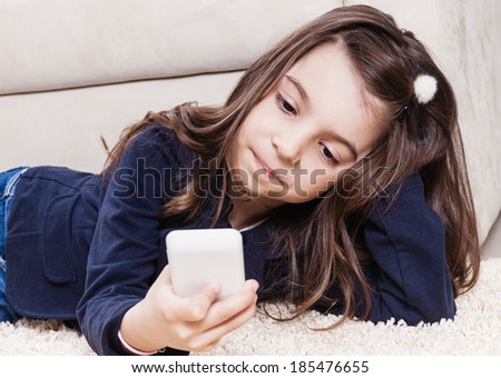 Toddler girl typing sms text message and lying on the floor