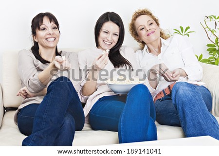 Three beautiful young women sitting on the sofa, watching tv