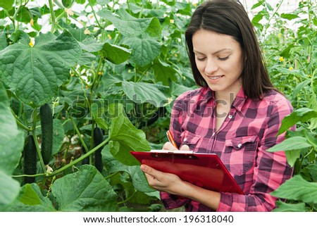 Young woman at work in greenhouse with clipboard in her hand