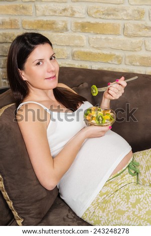 Pregnant woman lying in her living room and eating fruit salad.
