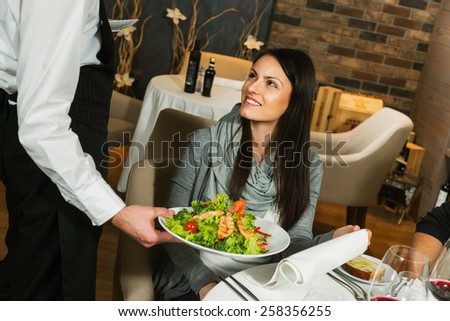 Waiter serving a plate of salad to a woman guest in a restaurant