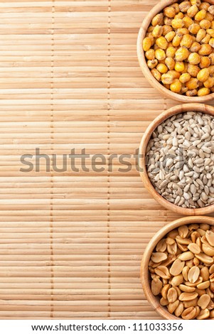 Three wooden bowls with roasted salted corn, sunflower seed and peanuts