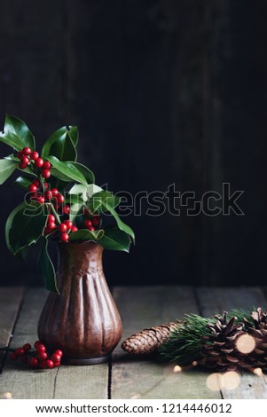 Christmas decorations, holly leaves with fresh red berries in vase.