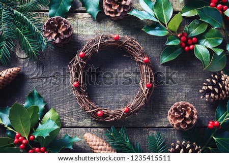 Making Christmas wreath using fresh and all natural materials. Christmas wreath with red berries and cones on wooden table.