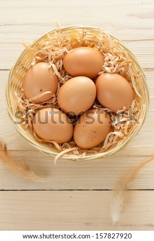 Basket of brown eggs with feathers on wooden table