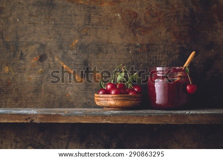 Jar of cherry jam and sour cherries on wooden shelf