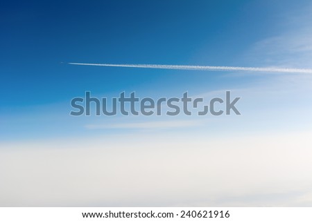 Side view of airplane contrail passing by against clear blue sky with sun flare