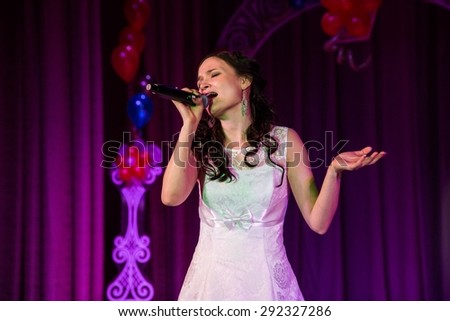 Singing woman in elegant dress with retro microphone. Beautiful glamour singer girl portrait with closed eyes against bokeh