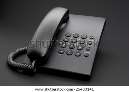Black office phone with cord isolated on black background