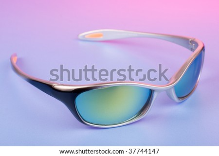 Fashionable sunglasses on color background under pink light