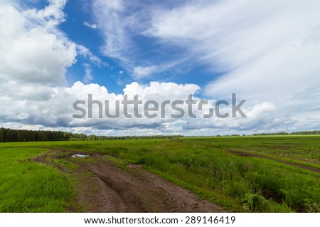 Rural field with clouds in the summer with a dirt road, Russia, Ural Mountains