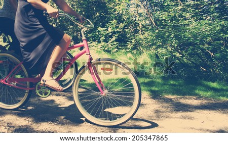 two ladies on bikes riding a bike path in motion on sunny afternoon with an instagram filter Focus is on first bike tire on pink bike
