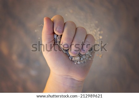 young girl hands with gravel and sand clinching and slowly dropping