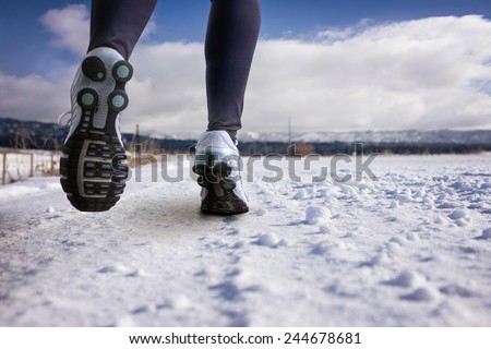 woman running on a snowy country road with view of the snow covered mountains in background on a sunny afternoon