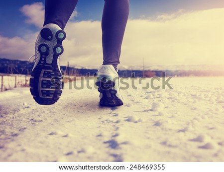 woman running on a snowy country road with view of the snow covered mountains in background with instagram filter (shallow depth of field)