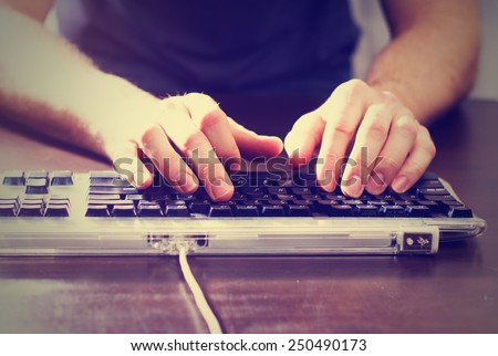 man typing at a tabletop with a black keyboard with a retro instagram filter (shallow depth of field)