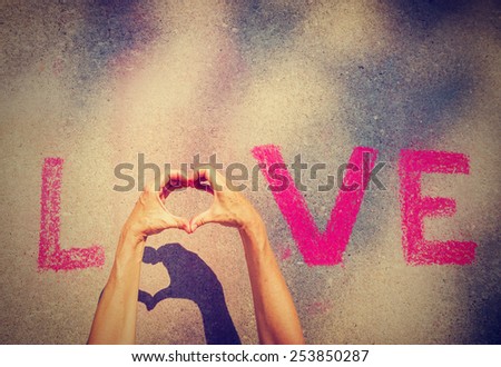 woman\'s hands creating the O in the word LOVE written in chalk and a shadow underneath the hands with a instagram filter (shallow depth of field)