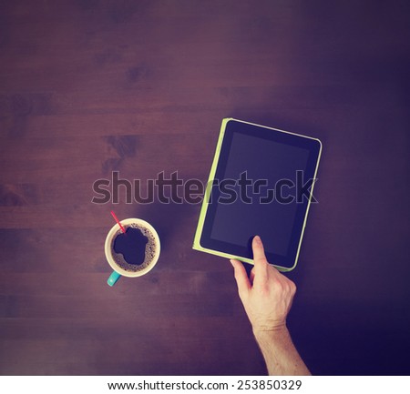 male hand touching tablet screen with finger tip with coffee cup and copy space with a retro instagram filter (shallow depth of field)