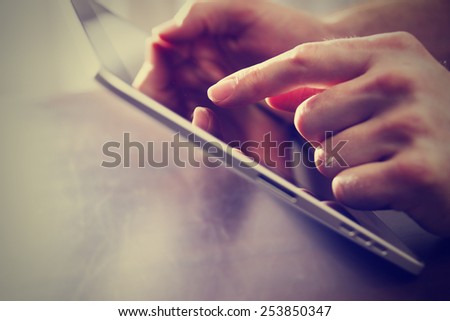 male hand touching tablet with finger tip while holding on a table with a retro instagram filter (shallow depth of field)
