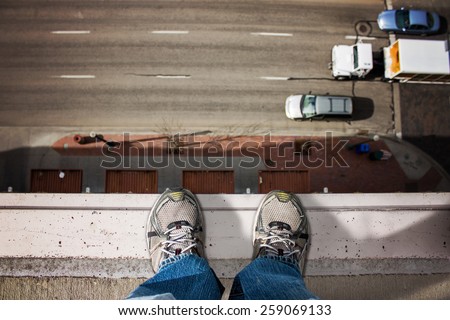 man standing on edge of tall building looking down upon the road with moving cars passing by below (shallow depth of field)