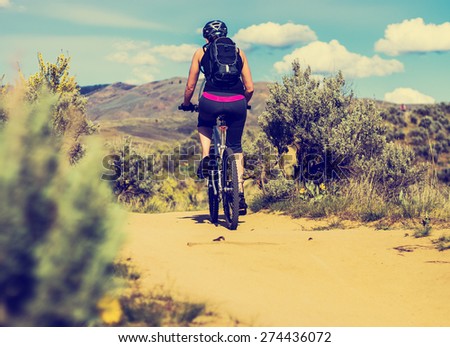 woman riding a mountain bike on a trail in the foothills during the late evening sun with a retro instagram filter (object is in motion)