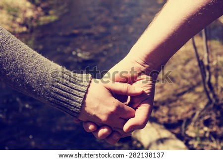 view of couple holding hands on a walk by a mountain stream with a retro instagram filter (shallow depth of field)