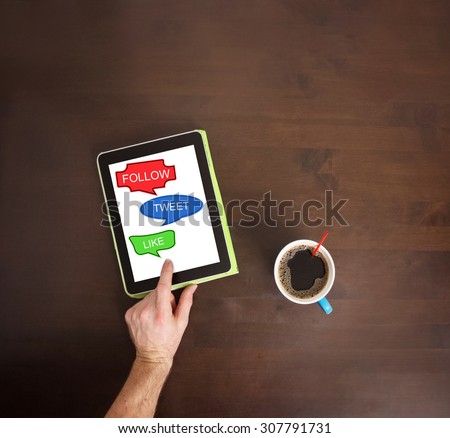 man working at a wooden desk on social media concepts with cup of coffee nearby (shallow depth of field)