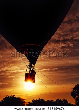 a silhouette of a hot air balloon pilot and balloon across an open fire sky