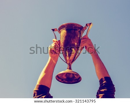 hands holding trophy up in the air with a shallow depth of field with a retro instagram filter