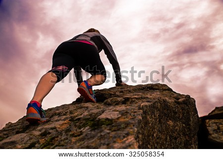 woman hiking and climbing over a large boulder to reach the top of a peak with a toned retro instagram filter