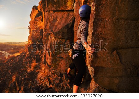 young woman bouldering and rock climbing on large cliffs during sunrise or sunset with a toned overlay filter
