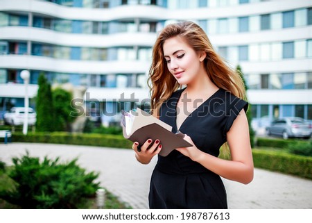 Beautiful young woman reads the address book on the street in a black suit
