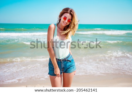 Portrait of a stylish sexy girl in sunglasses and jeans shorts. Resting on a paradise beach, enjoying the sun.