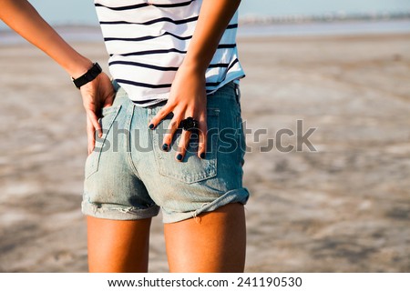 Sexy woman body in jean shorts. The model is back.Tan lady with perfect body posing outdoor. Wearing jeans stylish shorts and striped shirt .