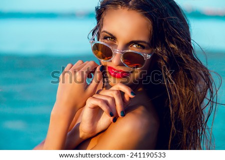 Young beautiful tanned fitness girl with beautiful big eyes and red lips posing on the  tropical evening beach . Wet hair and perfect skin .Close up portrait .